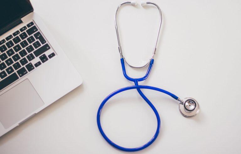 Blue stethoscope beside a laptop on a white surface