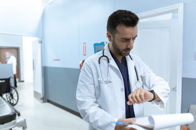 A doctor in a white lab coat checks his wristwatch in a hospital hallway, conveying professionalism