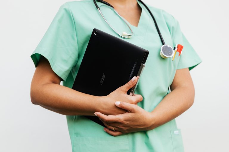 Close-up of a nurse in green scrubs holding a tablet and stethoscope, symbolizing modern healthcare