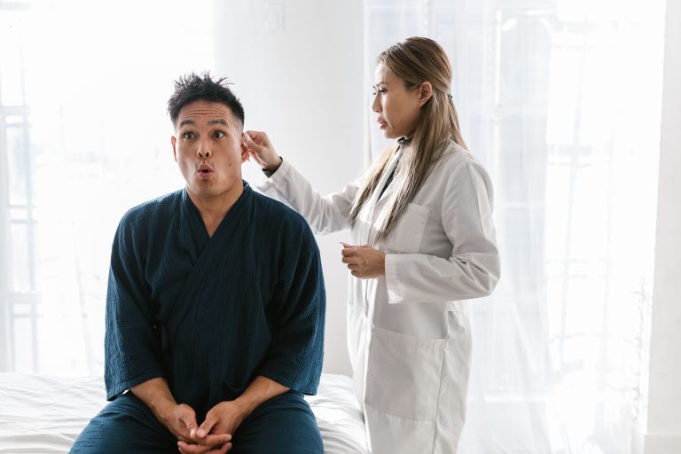 A doctor in a white coat conducts an ear exam on a patient indoors