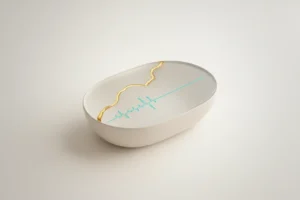 Sleek biometric sensor with a gold kintsugi seam and a calming waveform on a soft neutral background.