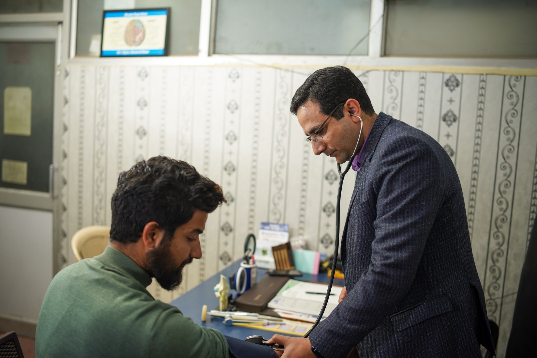 Clinician examining a seated patient with a stethoscope