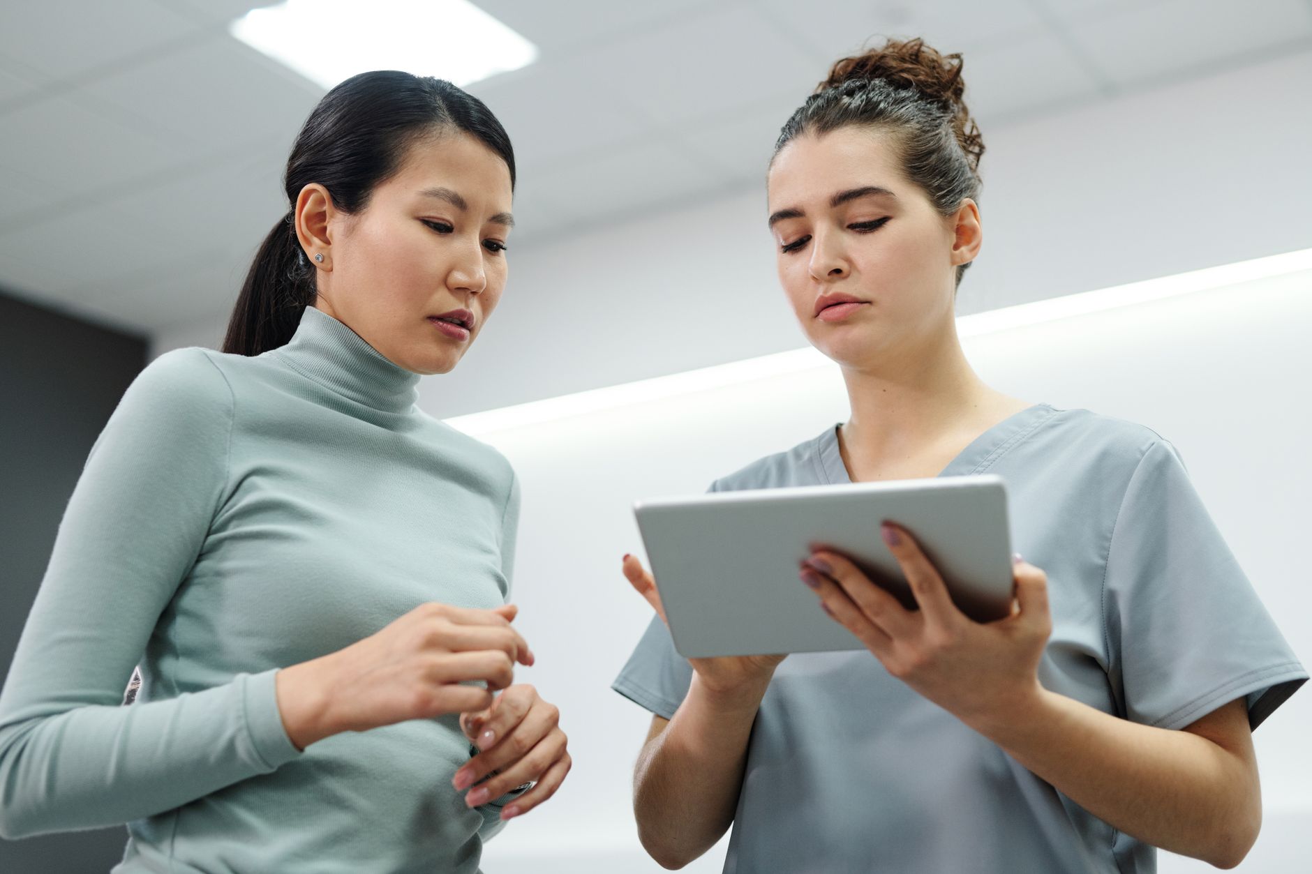 Two women engaged in a healthcare consultation using a digital tablet indoors
