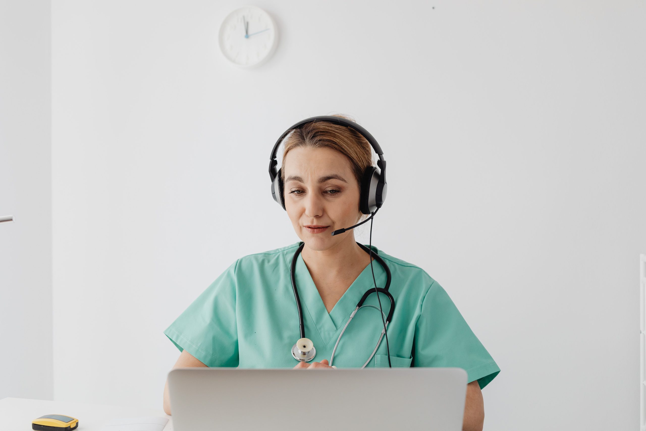 Clinician in green scrubs wearing a headset at a laptop