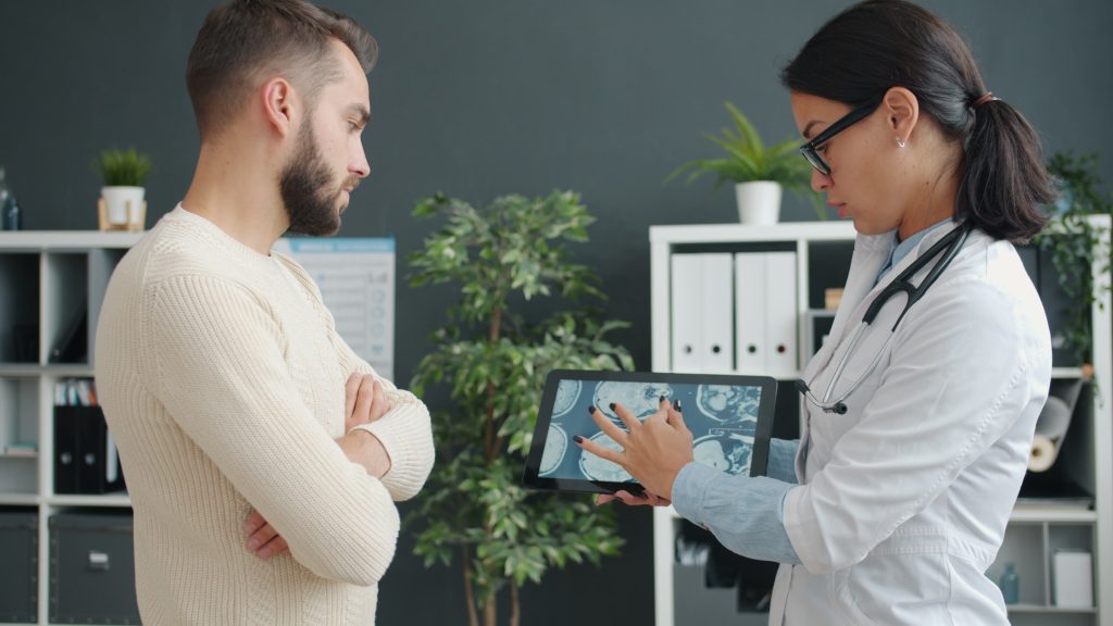 A doctor shows MRI scan to a worried patient using a tablet in a modern clinic