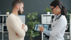 A doctor shows MRI scan to a worried patient using a tablet in a modern clinic