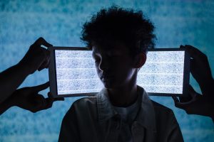 A teenager stands with eyes closed between two tablets showing digital noise, symbolizing information overload