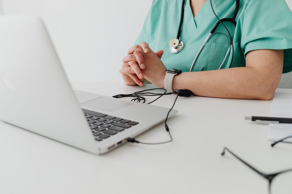 Medical practitioner in scrub suit using a laptop for remote consultation and documentation