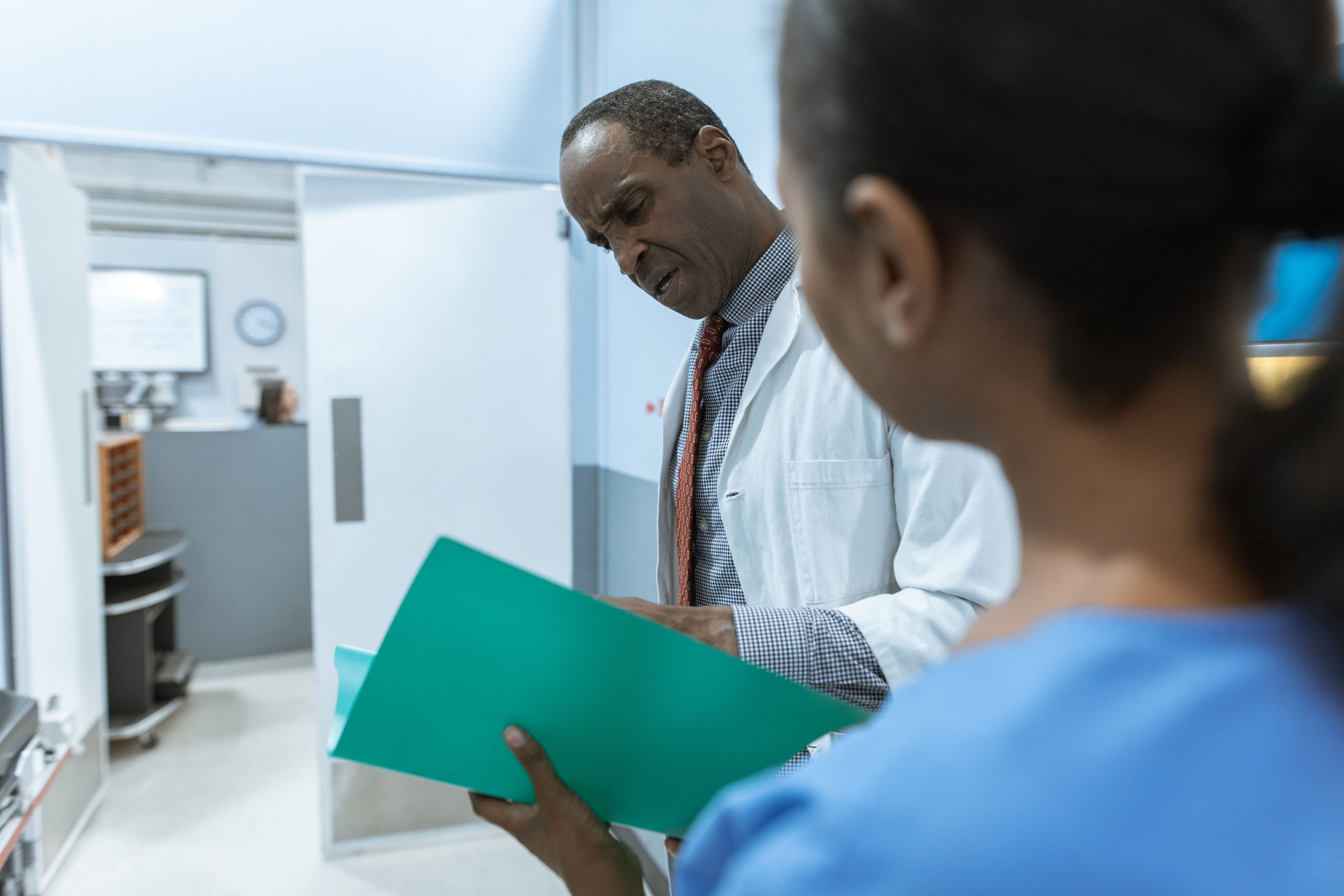 Clinician reviews a green medical folder with a colleague in a hospital room